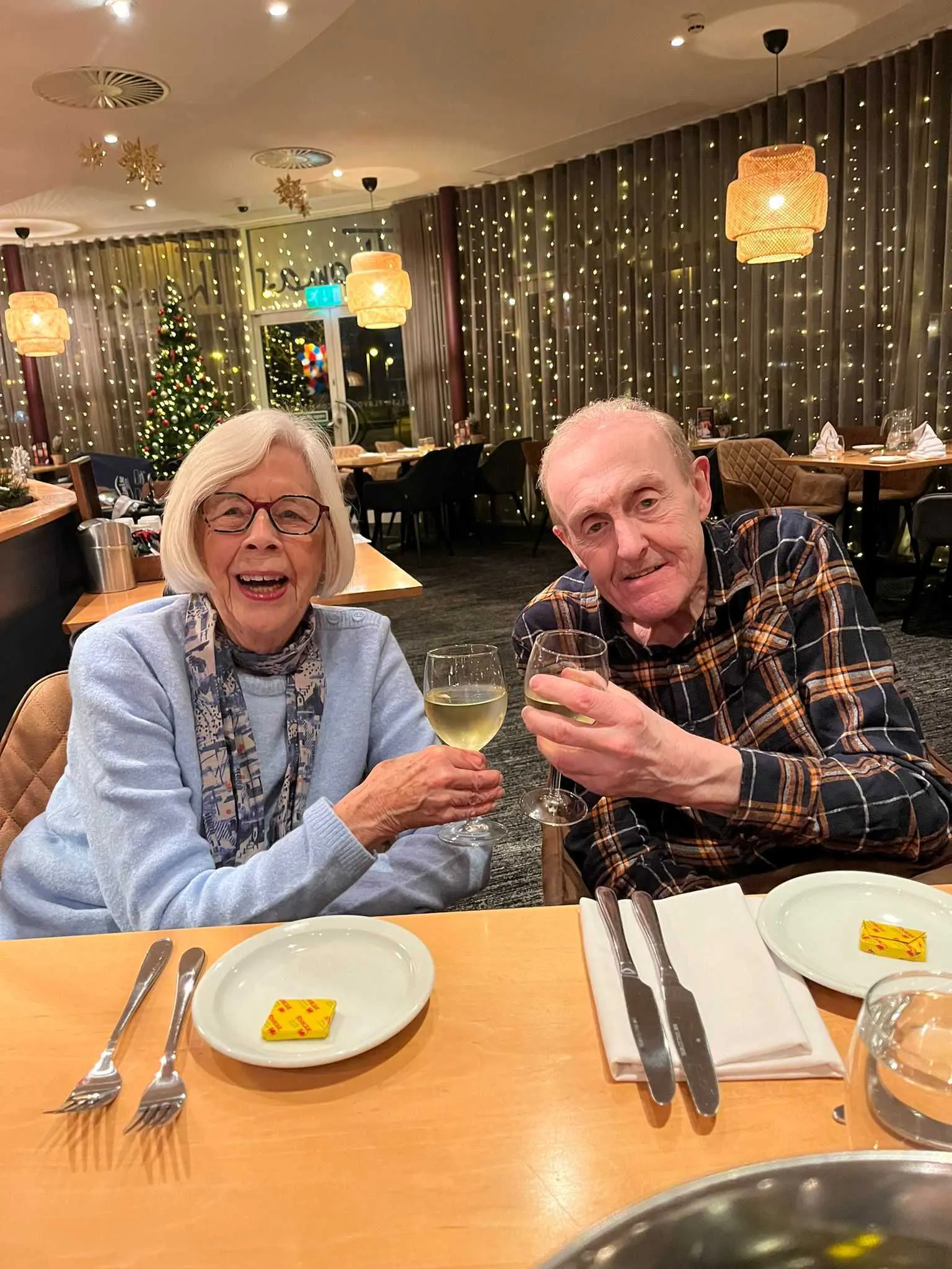 Two Limitless guests raise a glass over dinner at a Devon hotel, with fairy lights glowing behind them.