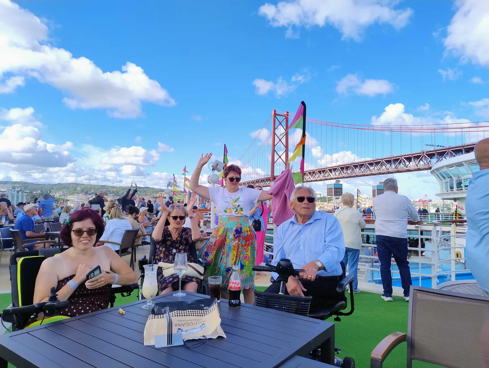 Limitless guests enjoy the sunshine at an outdoor table, with Lisbon's red suspension bridge behind them.